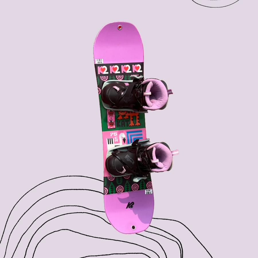 A toddler-sized Pink and green K2 snowboard with pink and black boots on a light purple background