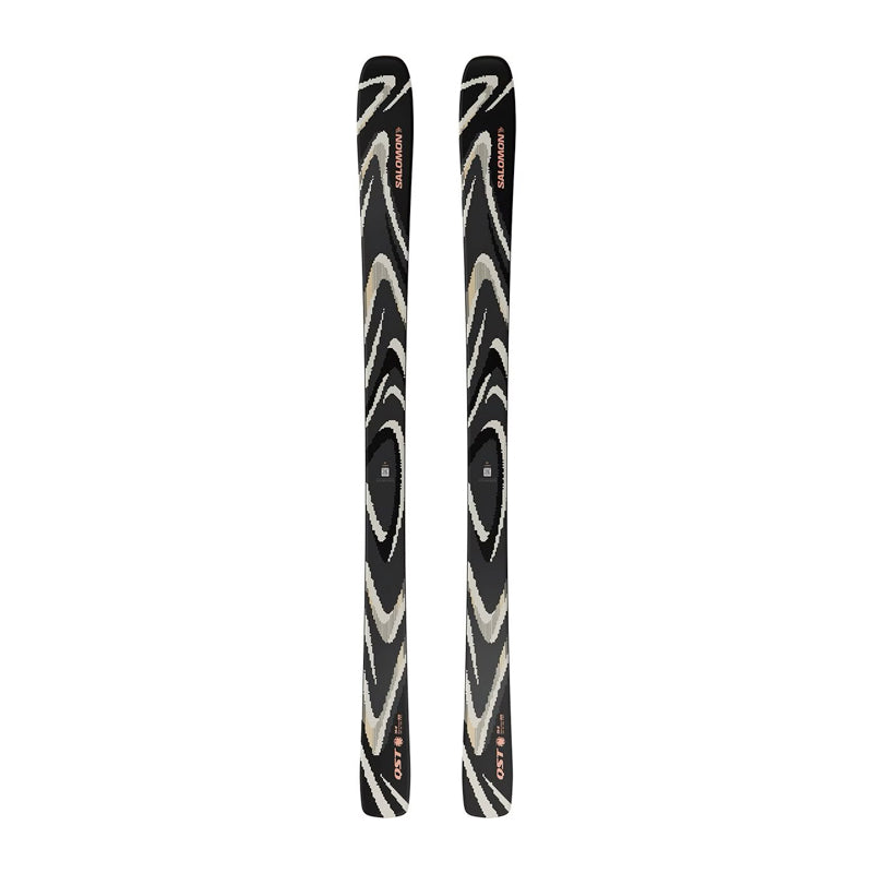 A pair of skis with a black base featuring a swirling zebra-like pattern in beige and white, with small red and orange logo details near the tips.