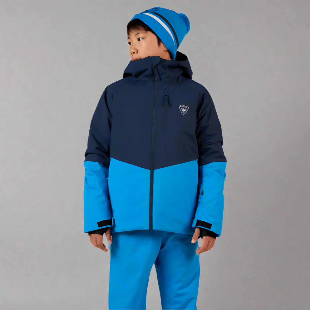 Child wearing a blue and navy ski jacket with matching pants on a white background