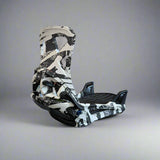 Black and white snowboard binding on a concrete surface with a brick wall in the background