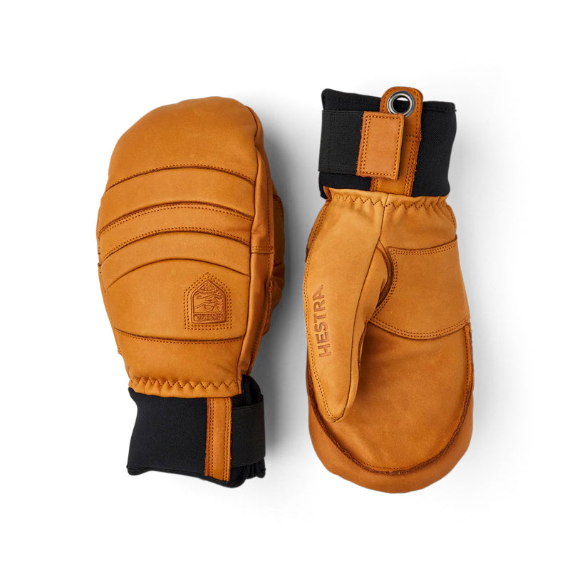A pair of tan leather winter mittens shown from both sides against a plain white background. One mitten is turned to show the back with stitched panels and a black cuff, while the other is turned to show the front with a black cuff and a vertical 'HESTR' brand name.
