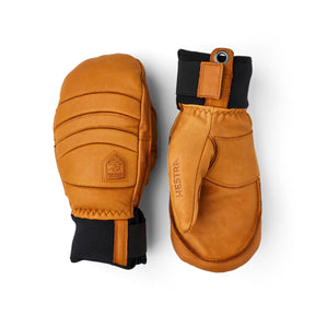 A pair of tan leather winter mittens shown from both sides against a plain white background. One mitten is turned to show the back with stitched panels and a black cuff, while the other is turned to show the front with a black cuff and a vertical 'HESTR' brand name.