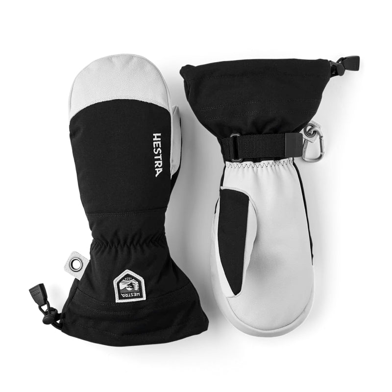 A pair of black and white winter mittens shown on a clean white background. One mitten is oriented to show the back with a black cuff, white finger tip, and a small white Heestra logo.