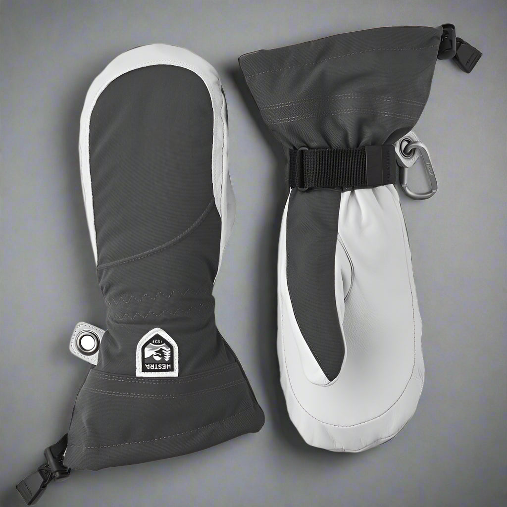 Pair of grey and white mittens with a visible Hestra logo on a grey background
